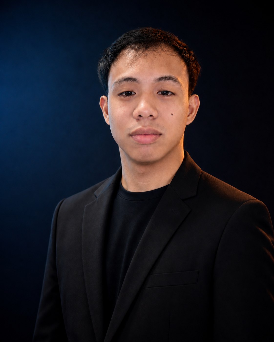 Portrait of Junry Virtucio wearing a black blazer against a dark studio background.